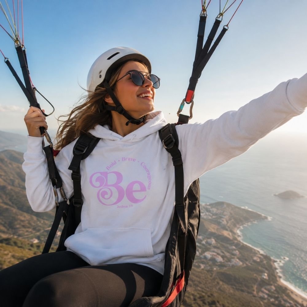 Woman paragliding while wearing the Be Bold Joshua 1:9 white Christian hoodie by The Avielle